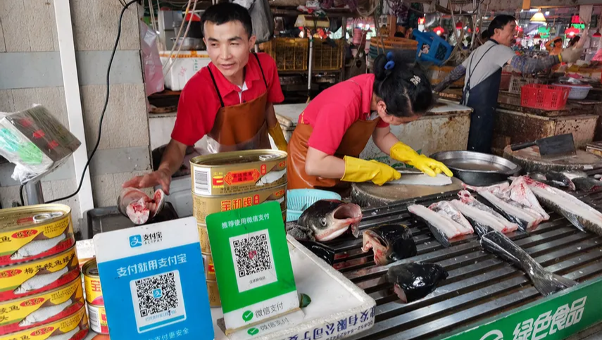 A traditional Chinese market with small vendors displaying QR codes for payments