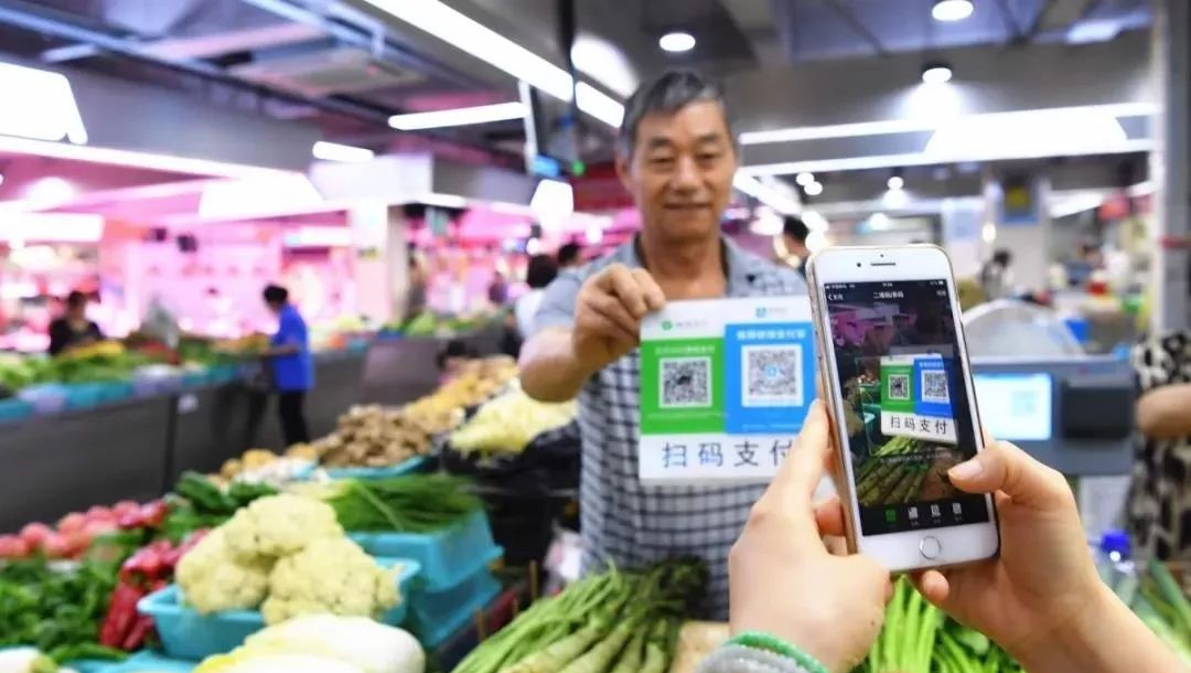 Crowded Chinese street market with vendors displaying QR codes for payment
