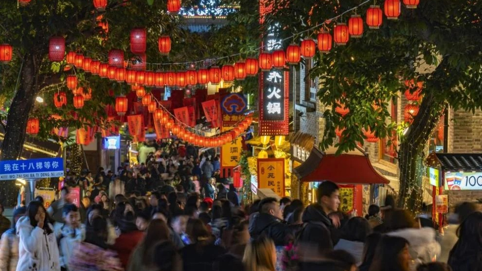 Happy tourists using mobile payments at a night market, with colorful lanterns in background