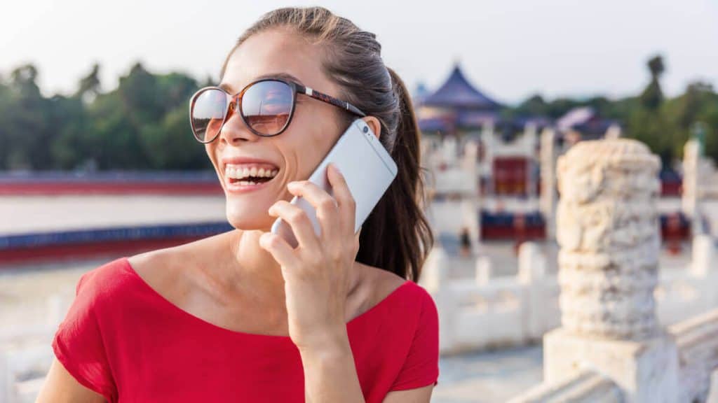 Happy traveler using smartphone with Chinese SIM card in front of Great Wall