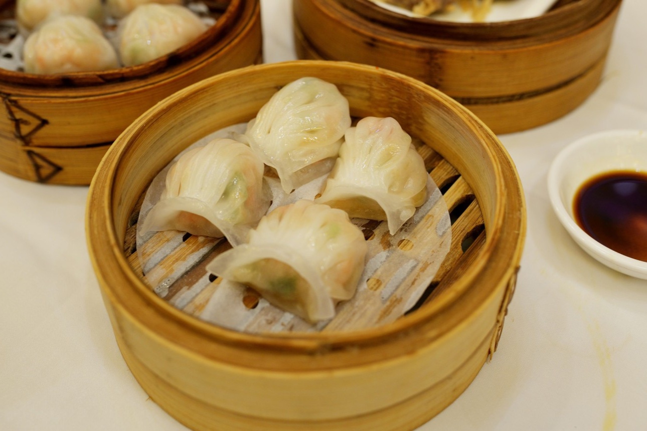  A close-up of the Har Gow Emperor (Shrimp Dumplings) in a bamboo steamer. The skin is visibly translucent, revealing the pink shrimp inside.