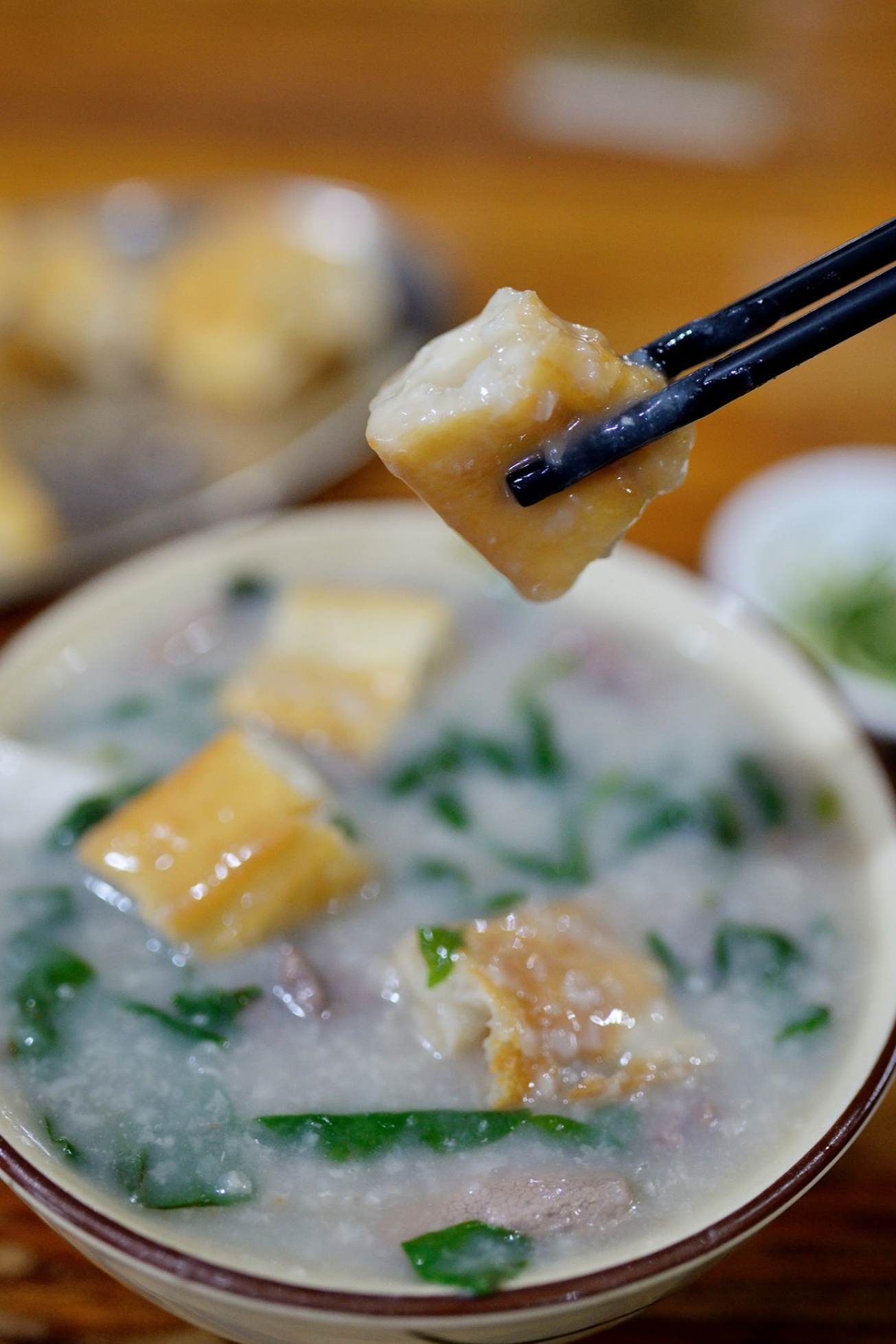  A hand holding a piece of youtiao, dipping it into the bowl of congee, illustrating the perfect way to enjoy it.