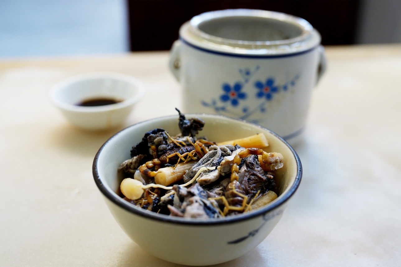  A scorpion from the soup held up on a spoon, ready to be eaten, highlighting the adventurous and delicious aspect of the dish.