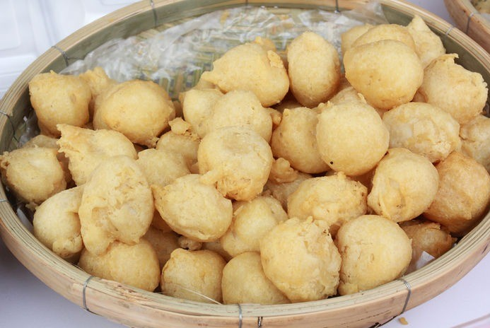  A small plate of golden-fried dace fish balls, with one cut open to show the springy texture, served alongside a small dipping saucer of clam sauce.