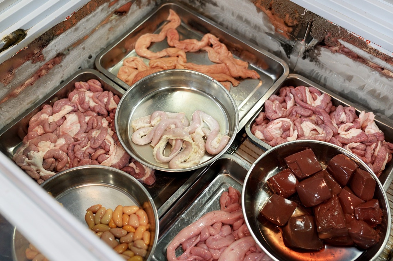  A vibrant, detailed shot of the large refrigerated display case, showcasing the neat rows of different types of glistening, fresh pork offal, ready for customers to choose.