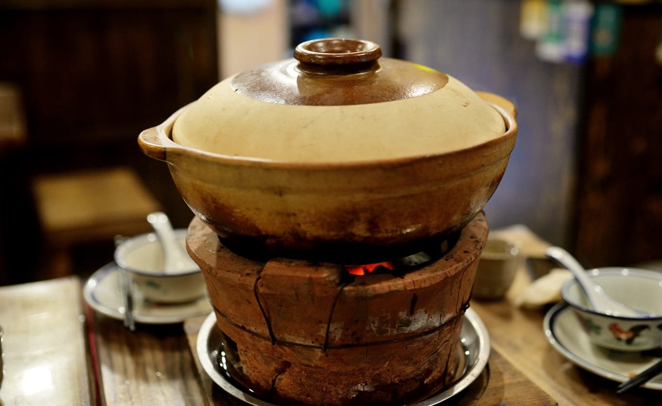 Traditional charcoal-fired claypot chicken cooking over a clay stove