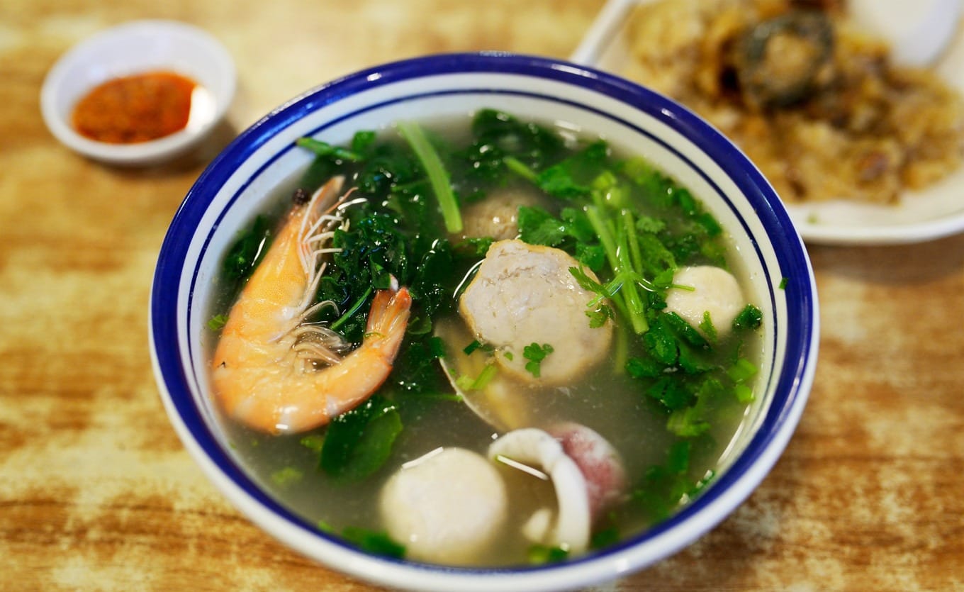 Fresh seafood soup with shrimp, squid, fish balls, meat rolls, and water spinach