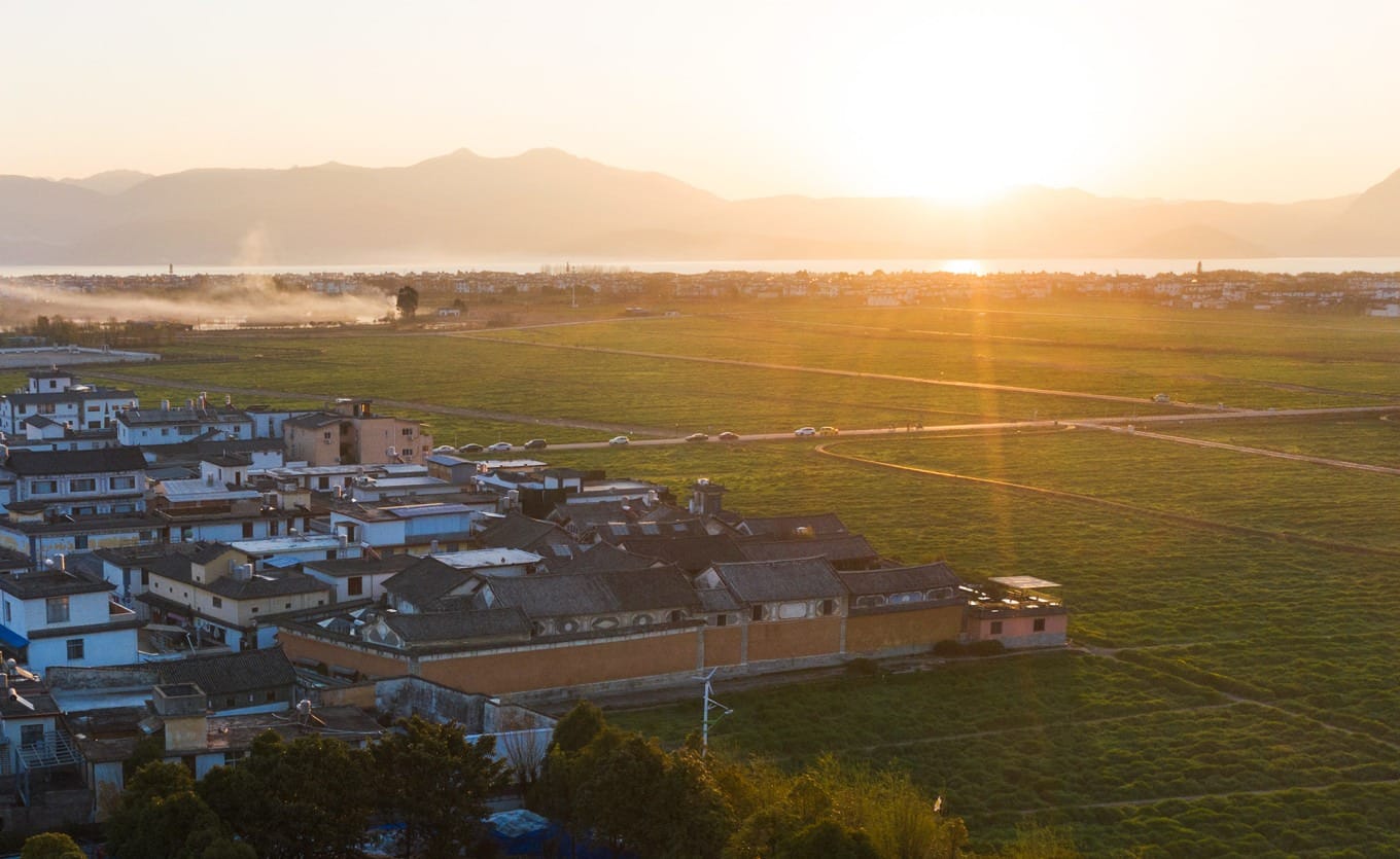 A narrow, cobblestone alley in Xizhou lined with traditional white-walled Bai houses with intricate wooden carvings