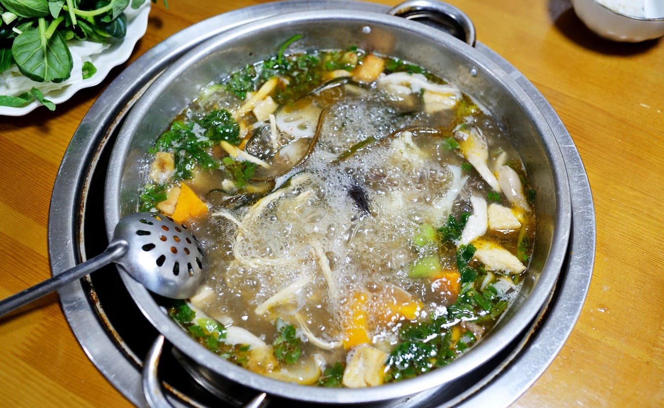 A close-up of tender beef and vegetables being dipped into a spicy, herbaceous sauce