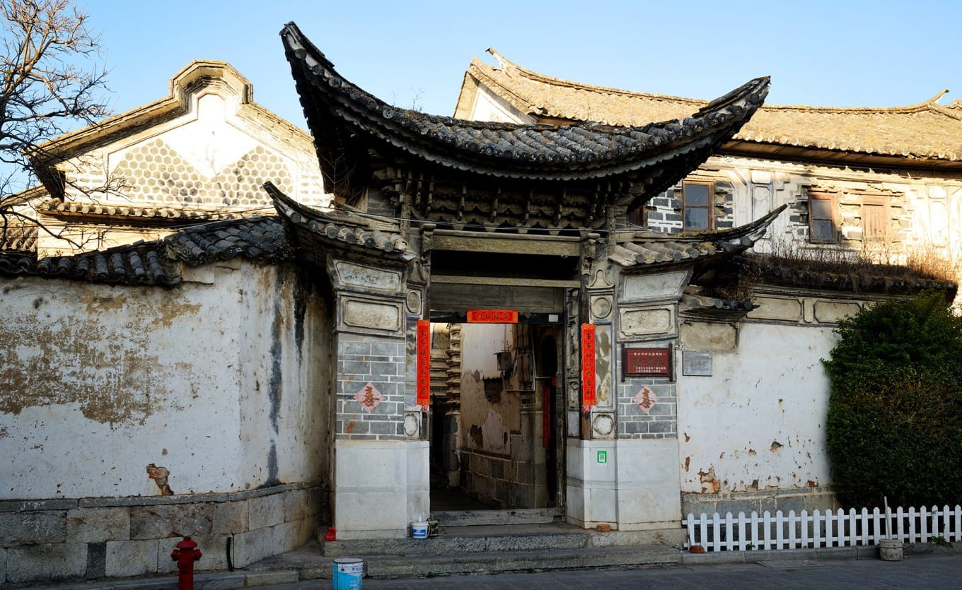 The Linden Centre (Xilin Yuan) seen across a vibrant green wheat field with its distinctive earth-yellow walls