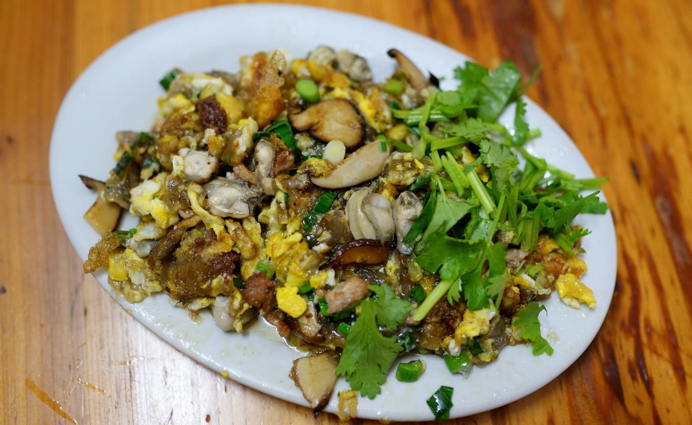 Chef preparing wet stir-fry oyster omelette with eggs and celery in a wok