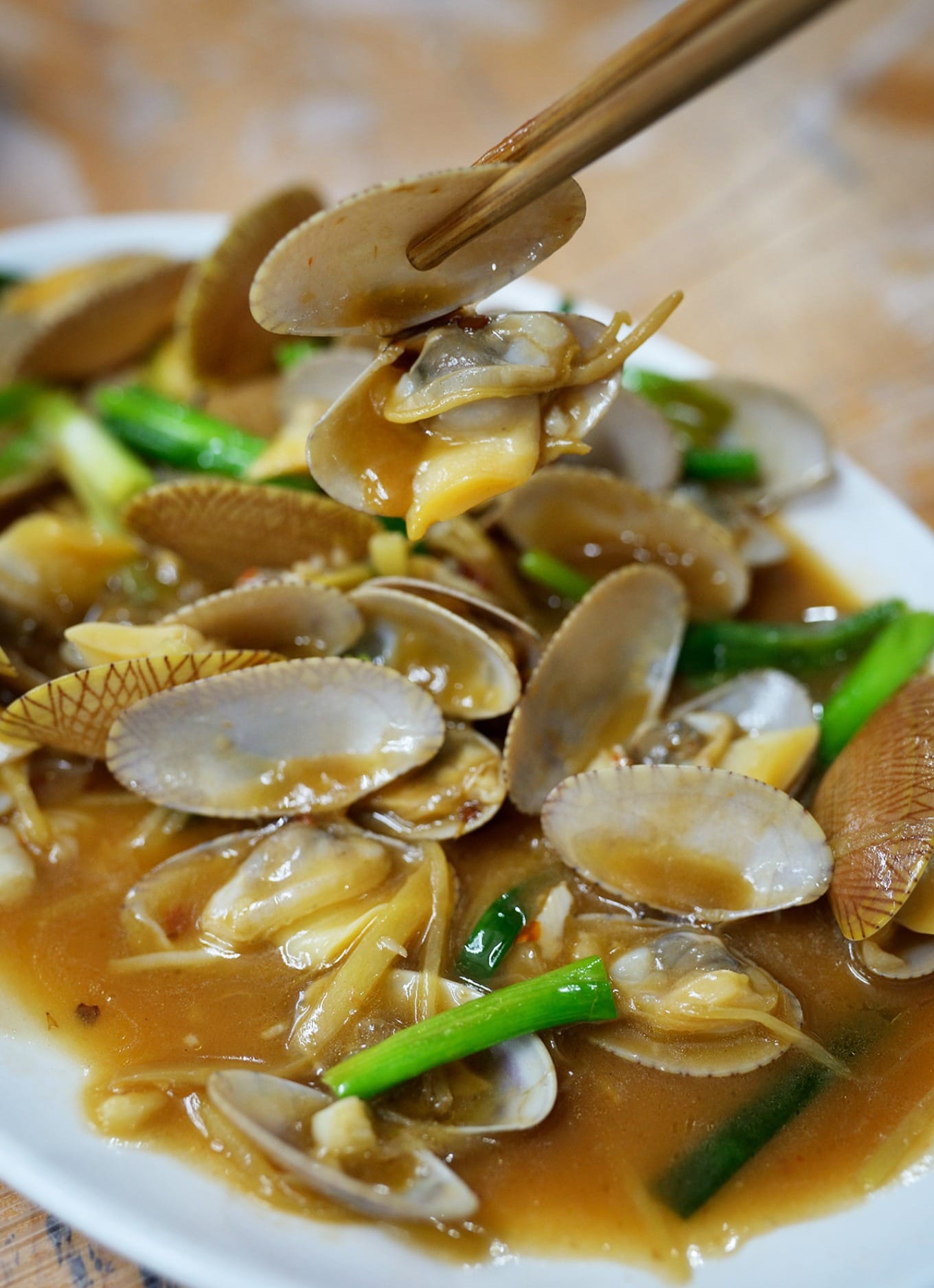 Ginger and scallion stir-fried clams served on a ceramic plate