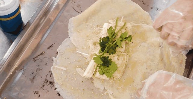 Vendor wrapping fresh sugar scallion in thin pancake with sesame and cilantro