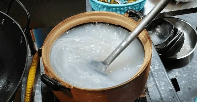 Chef adding fresh fish slices and shrimp to bubbling claypot porridge