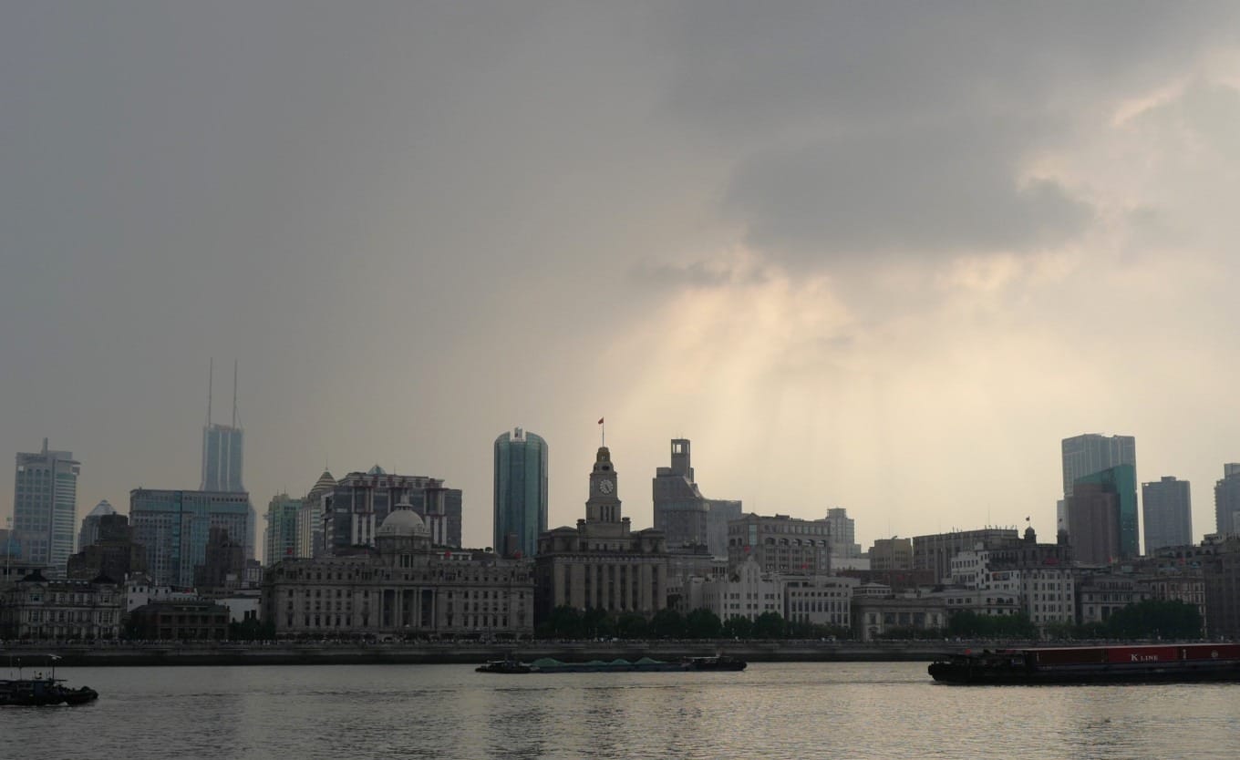 Crepuscular rays breaking through clouds over Shanghai's Huangpu River at dusk