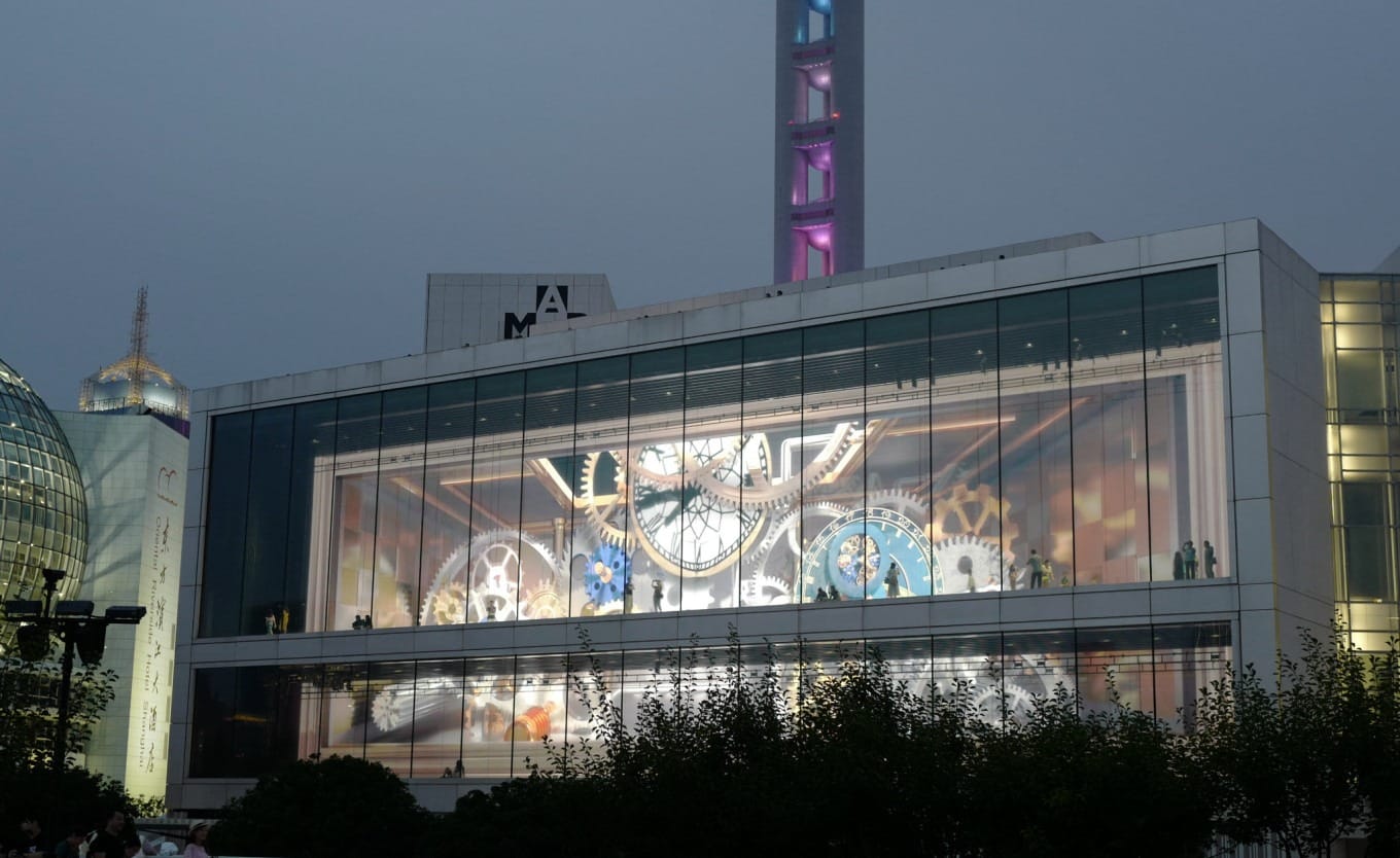 Visitors silhouetted against projected clockwork animation on Pudong Art Museum windows