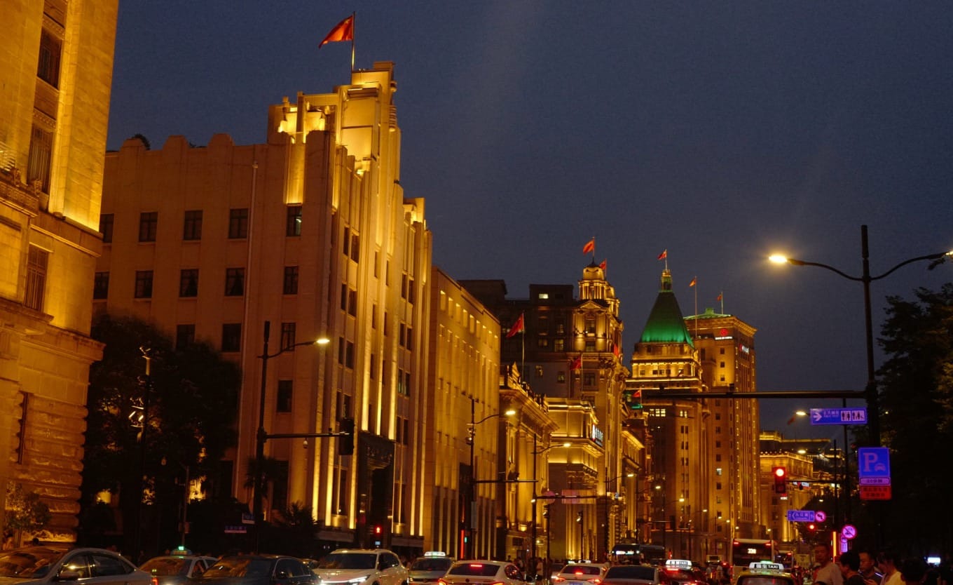 Double-decker sightseeing bus passing in front of The Bund buildings at night