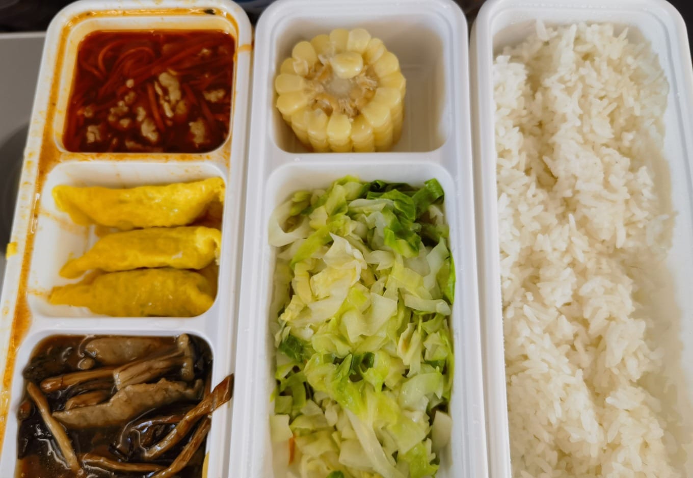 A boxed lunch on a high-speed train tray with rice, vegetables, and meat
