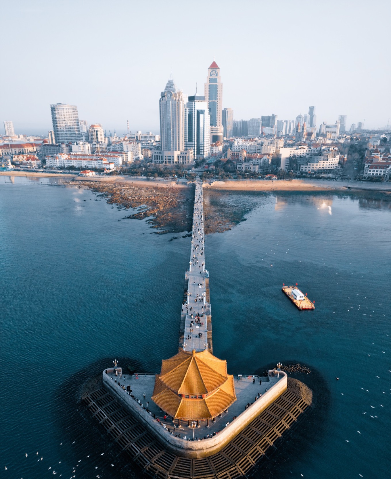 Golden sunrise over Zhanqiao Pier with calm sea and city skyline