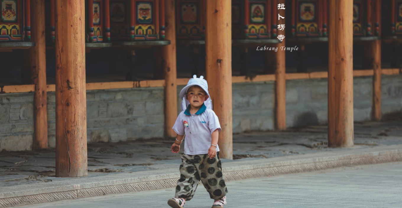 A young child reaching up to turn a large prayer wheel