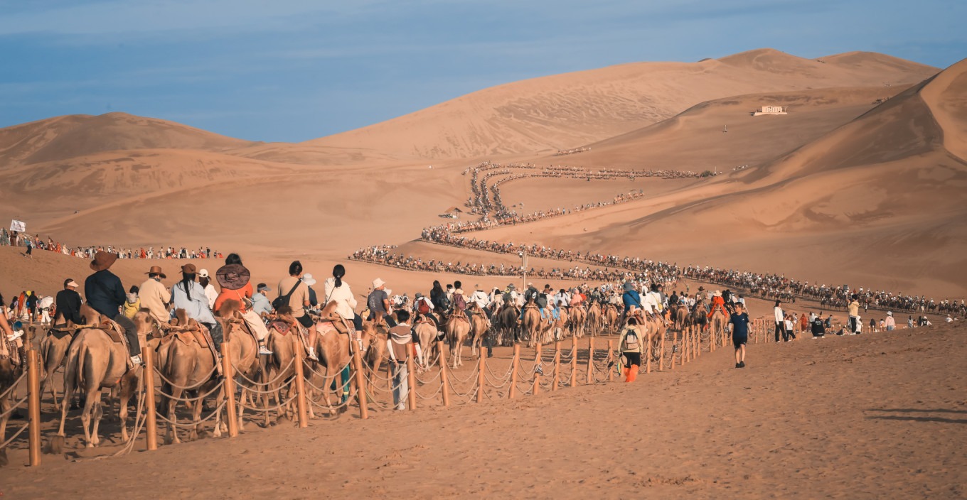 Crowds of tourists climbing the sand dunes and riding camels at Mingsha Mountain