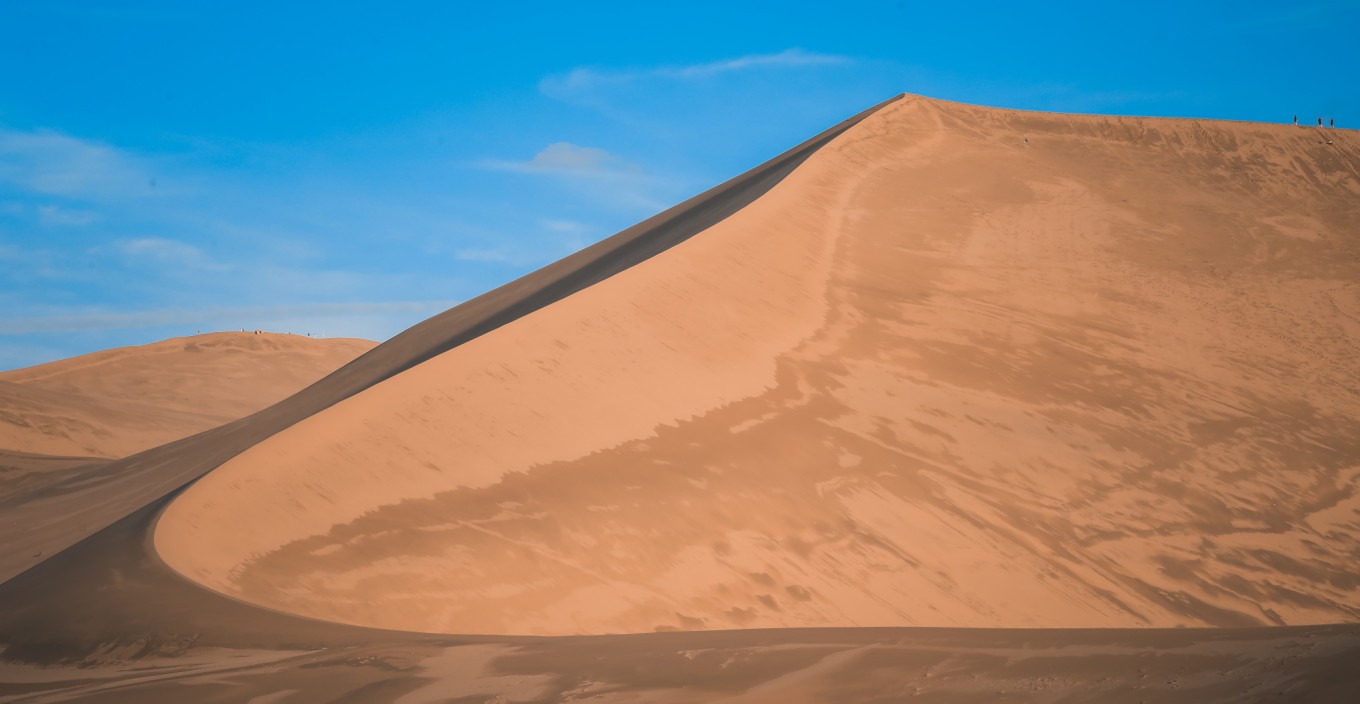 Wide-angle shot of sand dunes under a clear blue sky at Mingsha Mountain