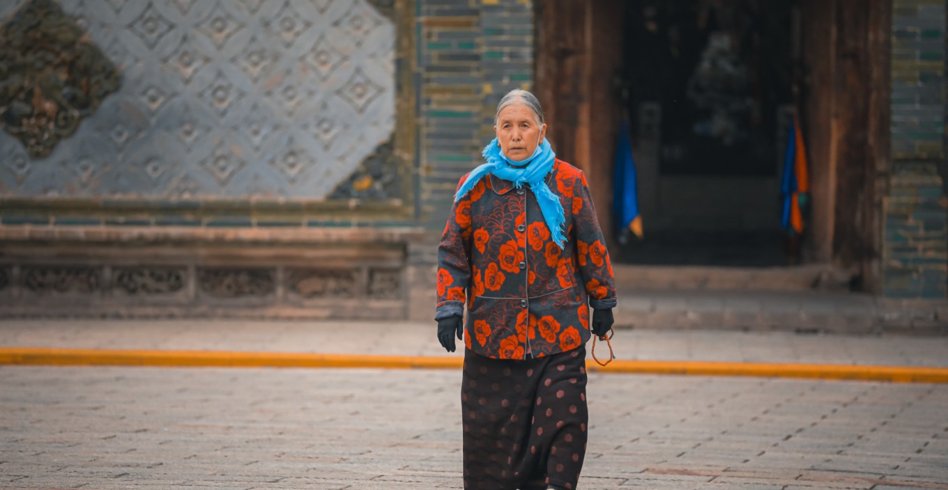 Elderly Tibetan woman in traditional dress walking in temple