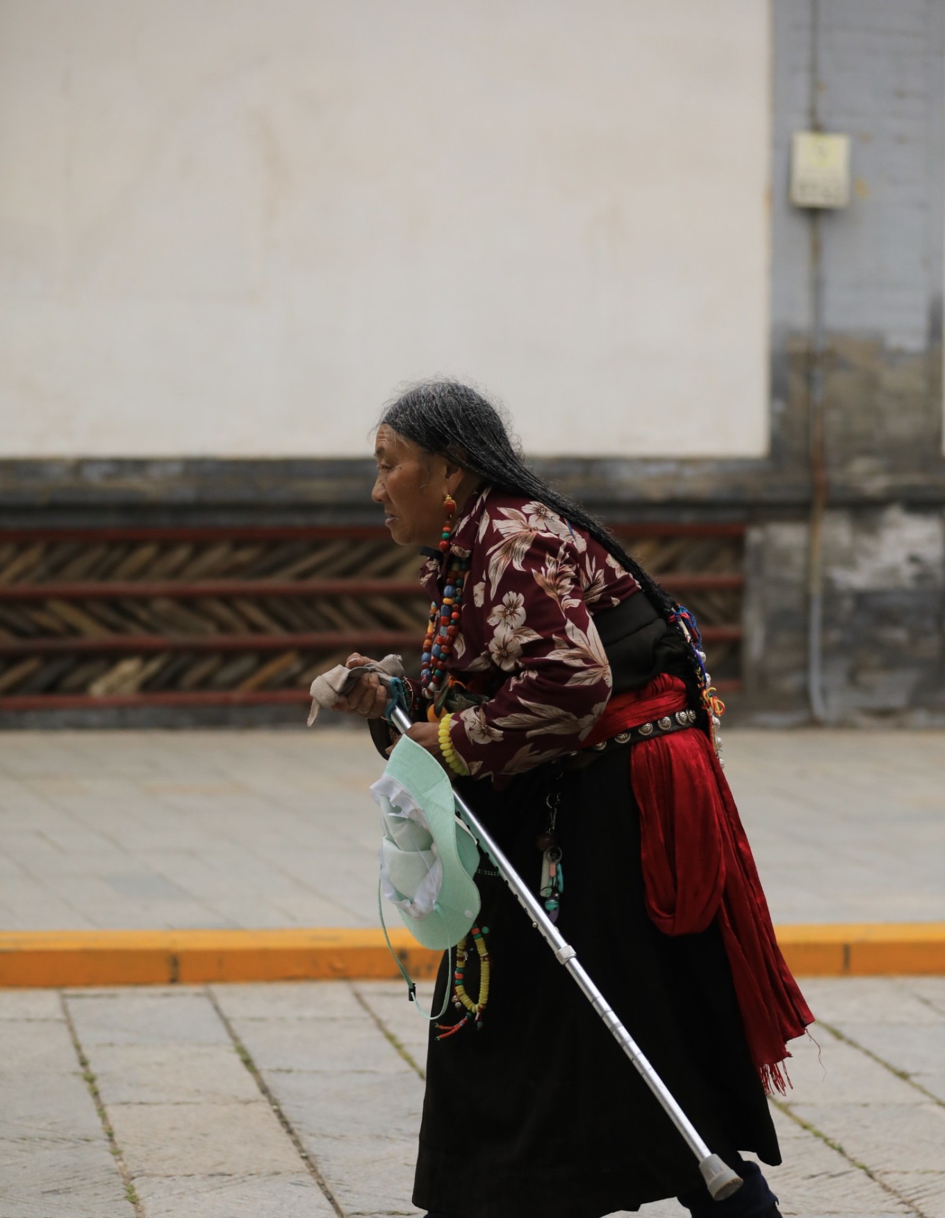 Bent figure of an old woman with a walking stick on stone path