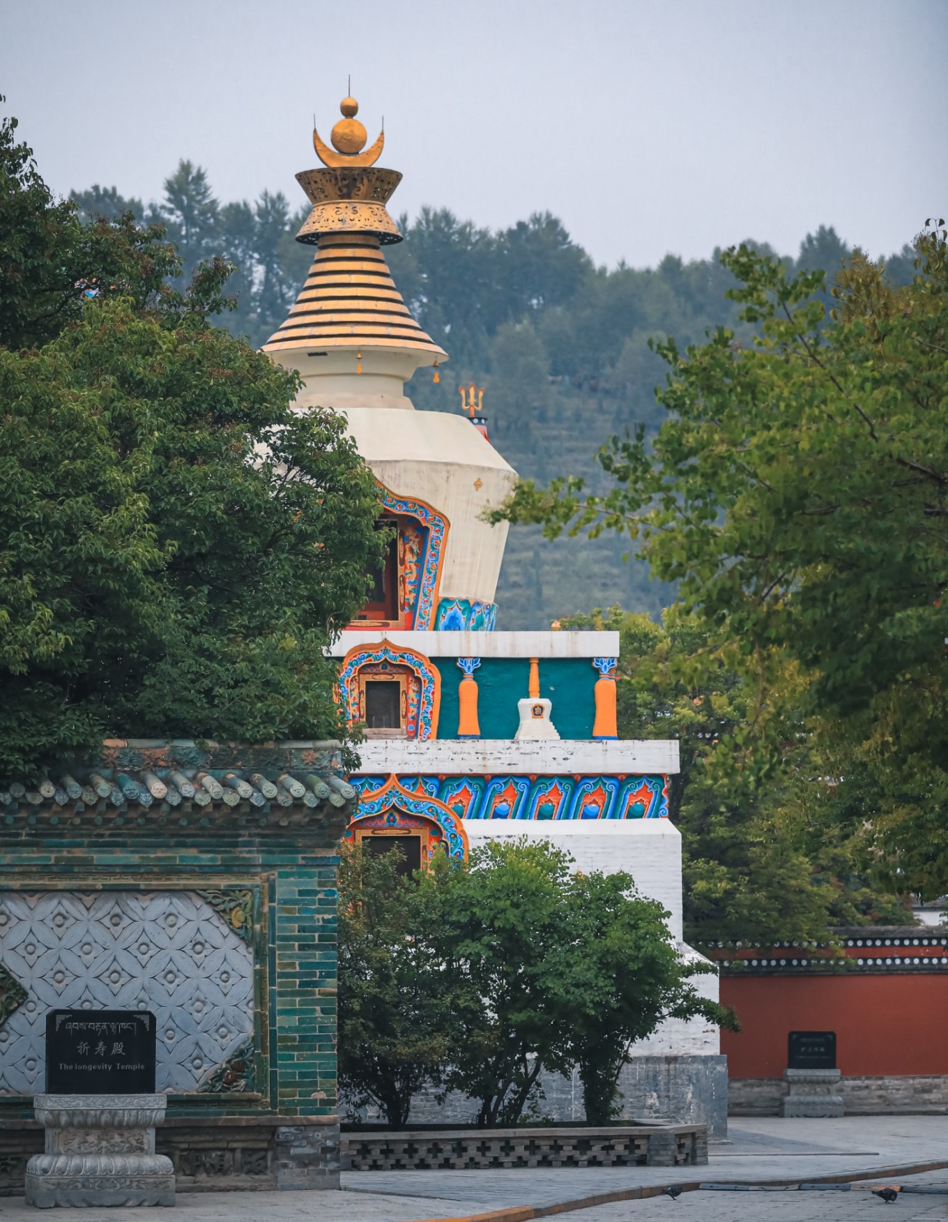 Woman in colorful Tibetan robe walking past white pagoda